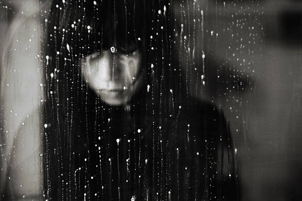 Mujer mirando ventana lluvia con melancolia.
